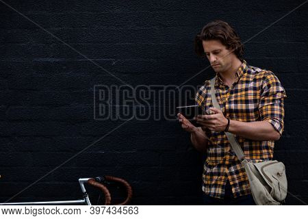 Front view of a young Caucasian man standing in the street holding a tablet computer with a bike next to him during his evening commute home