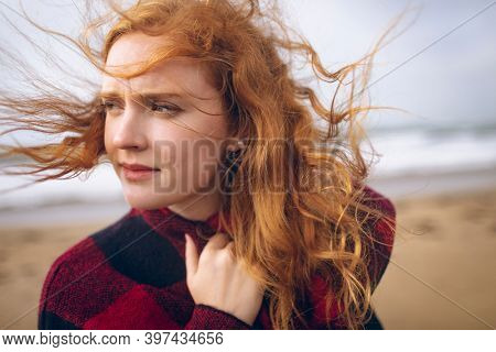 Thoughtful redhead woman standing in the beach