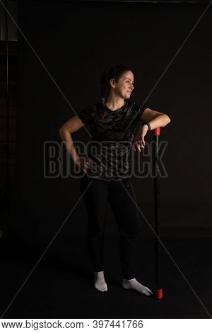 Fitness Woman Leans On The Bodybar Stretches Her Arms. Go In For Sports On A Black Background Cheerf