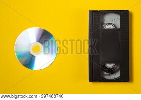 Video Cassette Videotape And Compact Disc On A Yellow Background. Flat Lay Concept.