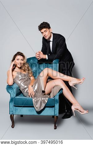 Elegant Young Couple Posing In Velour Armchair Isolated On Grey