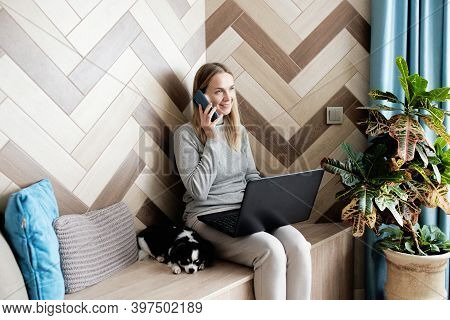 Adoult Woman 35s Working On Laptop And Talking On The Phone At Home, Cute Small Dog Besides. Work Fr