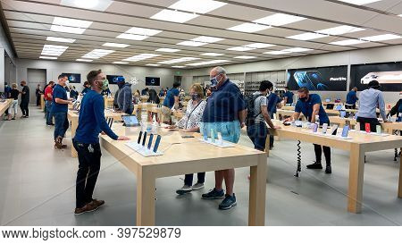 Salespeople And Customers At An Apple Store Looking At The Latest Apple Products For Sale.