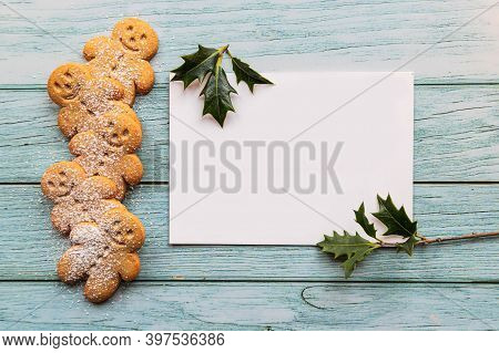 Gingerbread Cookies, Gingerman, Arranged On A Blue Table With Holly, Traditional Christmas Plant, An