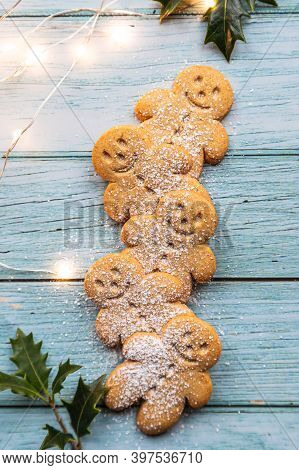 Gingerbread Cookies Or Gingerman Arranged On A Blue Wooden Table With Holly, Traditional Christmas P