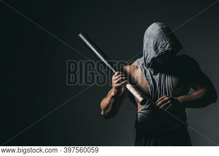 Dangerous Man In The Mask With Baseball Bat Ready For Fight. An Aggressive Muscular Hooded Man Is Ho