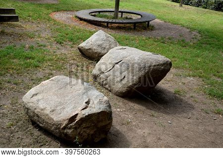 Three Round Boulders Of Gray Granite Lie On The Lawn In The Background A Wooden Circular Bench Aroun