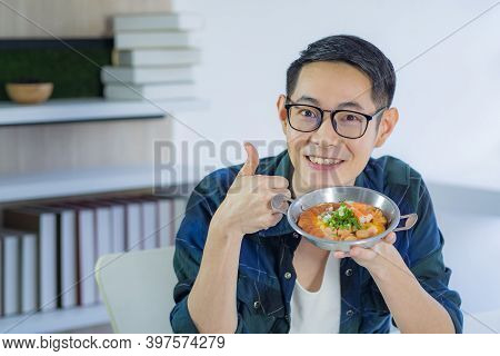 A Young Man Holding And Looking At The Fried Egg Served On A Pan With Colorful Toppings Served On A 