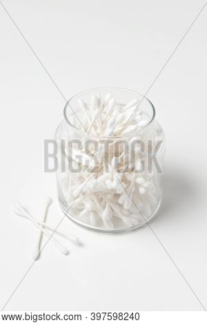 A glass jar full of Cotton Swabs with three on the white background.