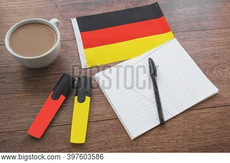 German National Flag, Pen, Notebook, Markers And A Cup Of Coffee On A Wooden Table, Foreign Language
