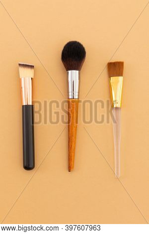 High angle view of three makeup brushes on yellow background. beauty grooming copy space concept.
