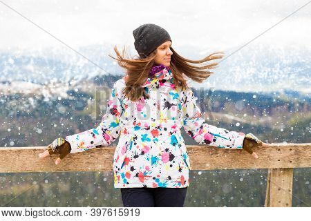 Happy Tourist Girl With Fly Hair In Colored Jacket Standing On Observation Deck In Mountains Covered