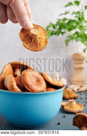 A Hand Taking A Rovellon From A Blue Bowl, Typical Autumn Mushrooms, With Ingredients For Its Prepar