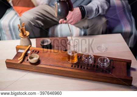 A Man Passes Hot Amber Tea From A Glass Flask Into A Cup. To Preserve Its Strong Flavor. Bamboo Tray