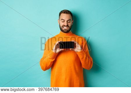 Image Of Man Cringe At Something On Mobile Screen, Staring Disgusted At Display, Showing Smartphone,