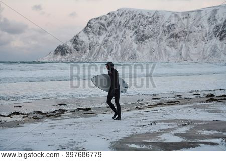 Arctic surfer going by beach after surfing