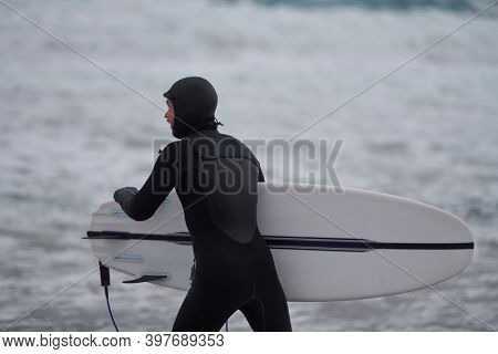 Arctic surfer going by beach after surfing
