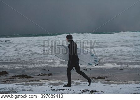 Arctic surfer going by beach after surfing