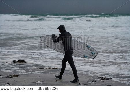 Arctic surfer going by beach after surfing
