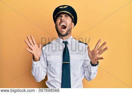 Handsome hispanic man wearing airplane pilot uniform celebrating mad and crazy for success with arms raised and closed eyes screaming excited. winner concept 