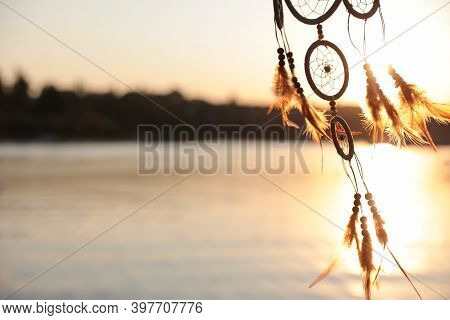 Beautiful Handmade Dream Catcher Near River On Sunny Day. Space For Text
