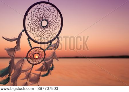 Beautiful Handmade Dream Catcher Near River At Sunset. Space For Text