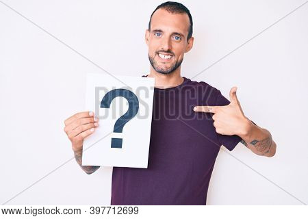 Young handsome man with tattoo holding question mark pointing finger to one self smiling happy and proud 