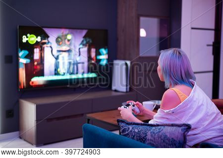 Teenager Girl With Colorful Blue And Pink Hair Hold Joystick And Play Video Games At Home At Night.