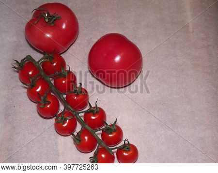 Two Large Tomatoes And Cherry Tomatoes On Branches Close Up On A Beige Background. High Quality Phot