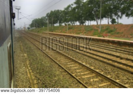Blurred Image Of Indian Rail Lines With Green Trees In The Side.