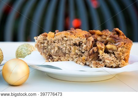 Golden Christmas Ball And A Piece Of Caramel Cake With Walnuts. White Table, Grey Chair And New Year
