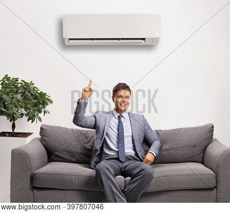 Professional man in a suit sitting under an air-contirioner and poiting up 
