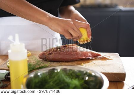 Mid section of chef grating lemon rind on roasted fish in restaurant kitchen. food preparation restaurant culinary gourmet