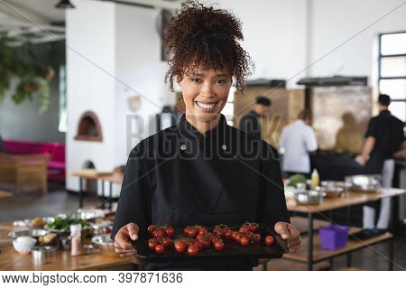 Female chef and divserse group in kitchen. portrait of female trainee chef smiling with trainee chefs standing and listening to female chef in the background.