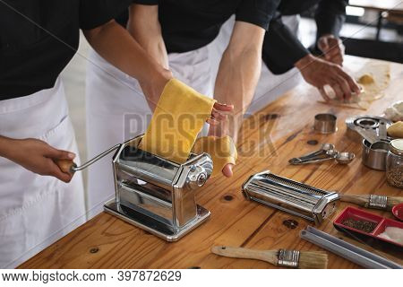 Mid section of male and female chef processing pasta sheet in machine at restaurant kitchen. food preparation restaurant culinary gourmet