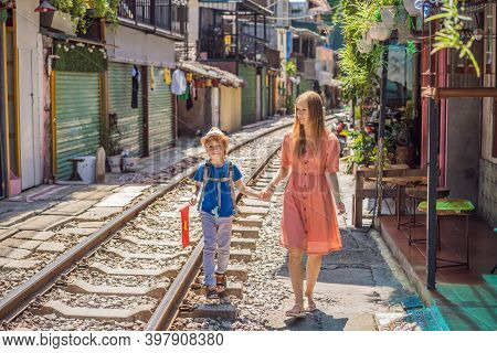 Mother And Son Travelers Walk Around Railway Paths Which Go Through Residential Area In Hanoi City. 