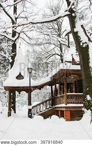 The Old Wooden House Is Covered With Snow And Ice. Icicles Hang From The Roof.