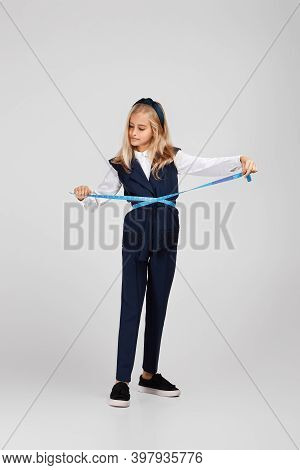 Happy Little Girl Holding Tape Measure On Studio Background. Full Lenth. Child Measures His Waist An