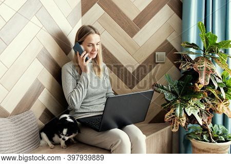 Adoult Woman 35s Working On Laptop And Talking On The Phone At Home, Cute Small Dog Besides. Work Fr
