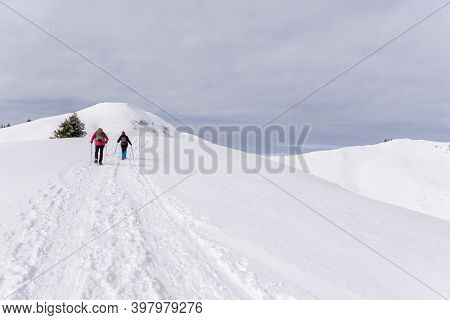 Senior Couple Is Snowshoe Hiking In Alpine Snow Winter Mountains. Allgau, Bavaria, Germany.