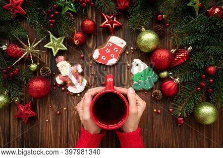 Woman Holding Hot Christmas Tea Against Decorations On Wooden Table. Top View. New Year Or Christmas