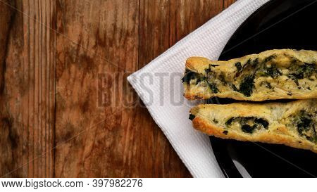 Rollini With Brynza Cheese And Spinach On A Black Plate With A Wooden Background