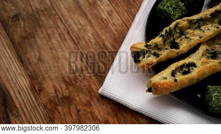 Rollini With Brynza Cheese And Spinach On A Black Plate With A Wooden Background. Green Squares Of D