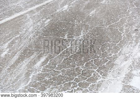 Cracks On The Asphalt Filled With Snow. Low Drifting Snow On Winter Road Texture Background