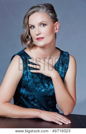 Mooie veertig jaar oude vrouw met fashion make-up, krullend kapsel op grijs blauw studio achtergrond.