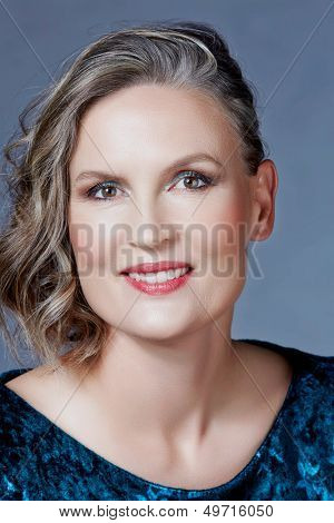 Mooie veertig jaar oude vrouw met fashion make-up, krullend kapsel op grijs blauw studio achtergrond.