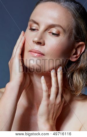 mooie veertig jaar oude vrouw met natuurlijke make-up en gezonde huidtextuur raken van haar gezicht op bl