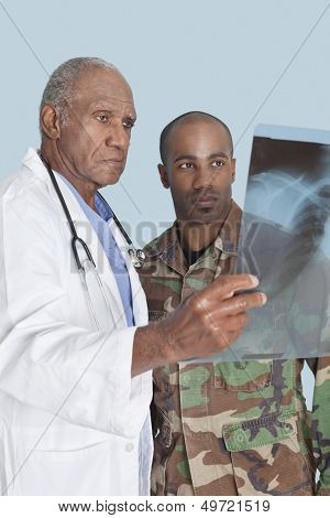 Senior doctor with US Marine Corps soldier looking at x-ray report over light blue background