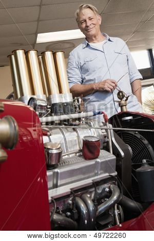 Close up of car engine with happy senior man standing behind