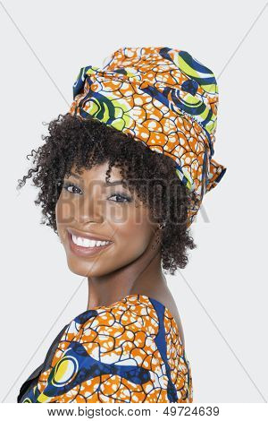 Portrait of young woman in African print attire looking over shoulder against gray background